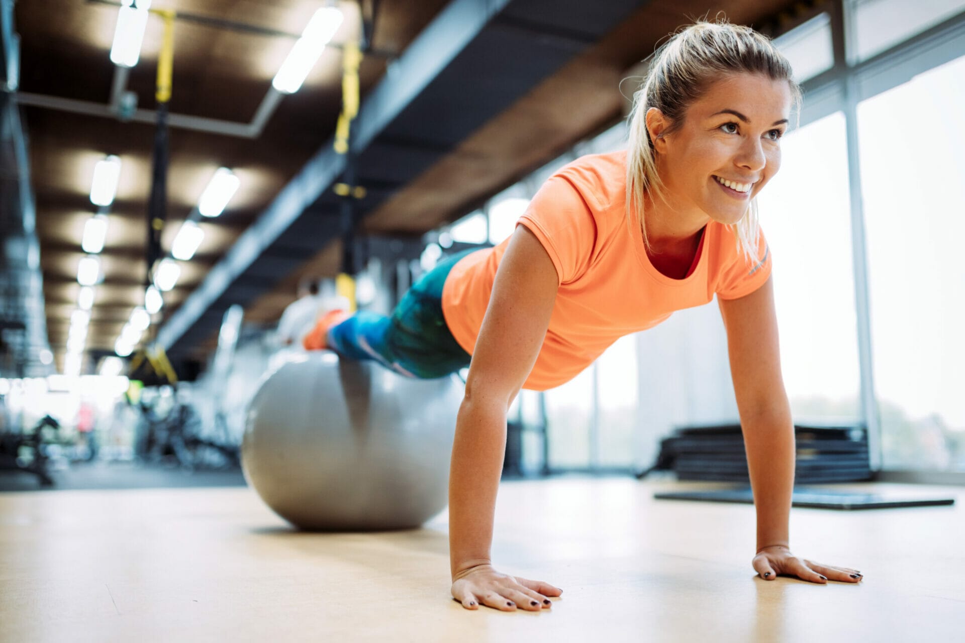 Young attractive woman doing push ups using ball in gym